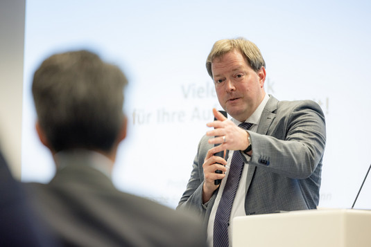 Prof. Dr. Stefan Greiner mit Mikrofon in der Hand, im Vordergrund ein Zuhörer.