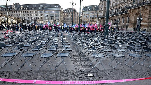 500 leere Stühle auf dem Hamburger Rathausmarkt, dahinter Teilnehmer der Streikaktion.